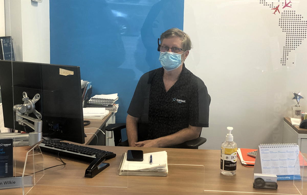 A masked travel advisor greets customers behind Plexiglass in Ontario. (Supplied)